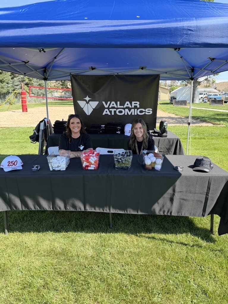 Two Valar Atomics staff at the giveaway table under a tent
